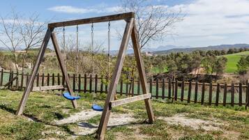 A wooden swing set in a grassy area with a wooden fence and trees in the background.