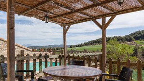 Une terrasse en bois avec une table et des chaises, donnant sur une piscine et un paysage pittoresque.