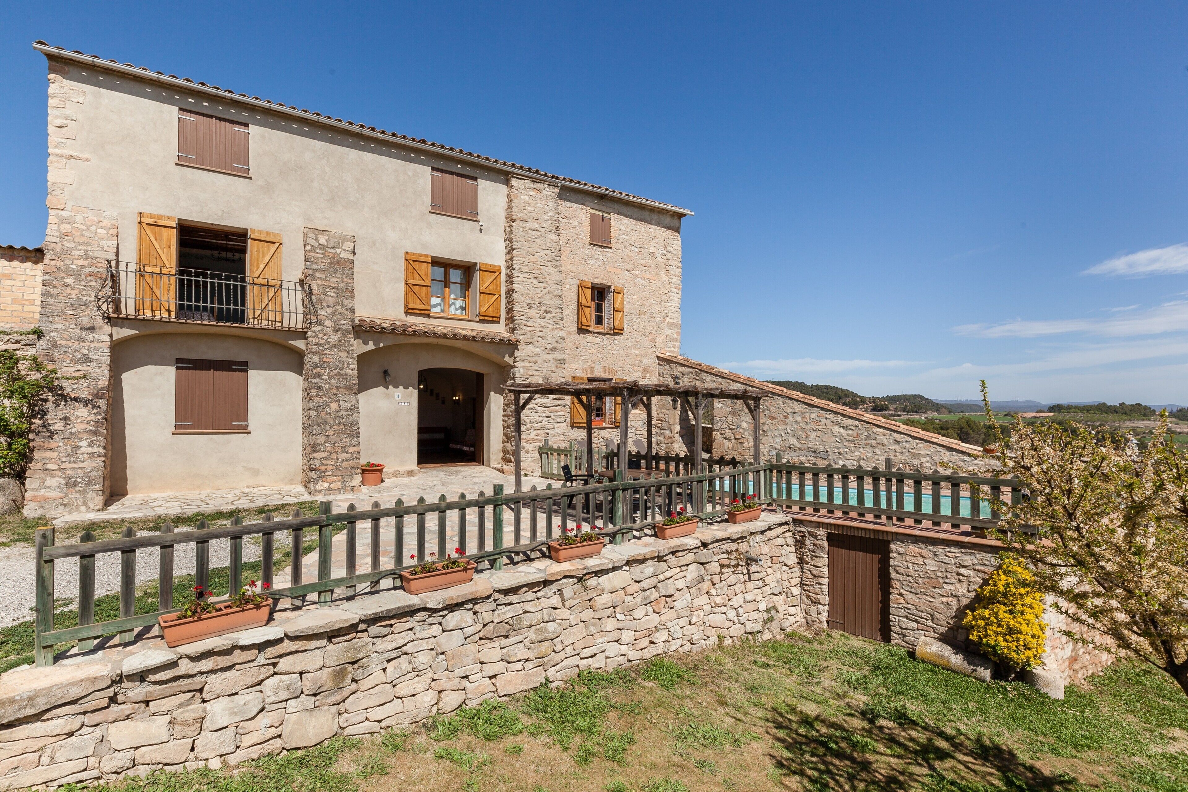 A stone building with a balcony, a pool, and a stone wall.