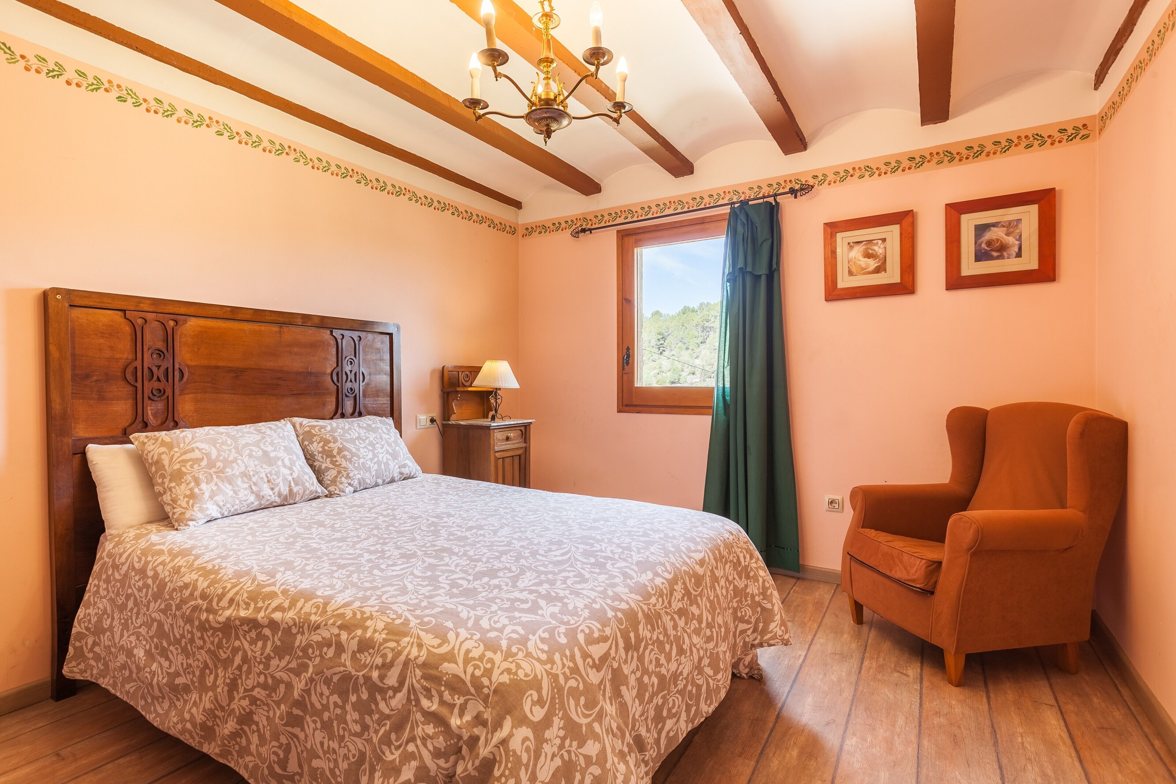 Un dormitorio con una cama de madera, una silla, un ventanal con cortinas e imágenes enmarcadas en la pared.