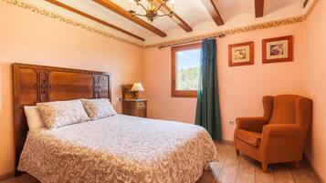 Un dormitorio con una cama de madera, una silla, un ventanal con cortinas e imágenes enmarcadas en la pared.