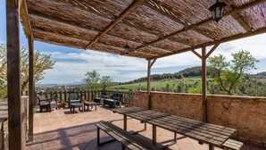 Een terras buiten met houten tafels en stoelen, een stenen muur en uitzicht op een groen landschap.
