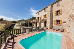 Ein Steinhaus mit Pool, Sitzgelegenheiten im Freien und einem Holzzaun.