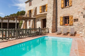 Un bâtiment en pierre doté d’une piscine, de volets en bois et d’une clôture en bois.
