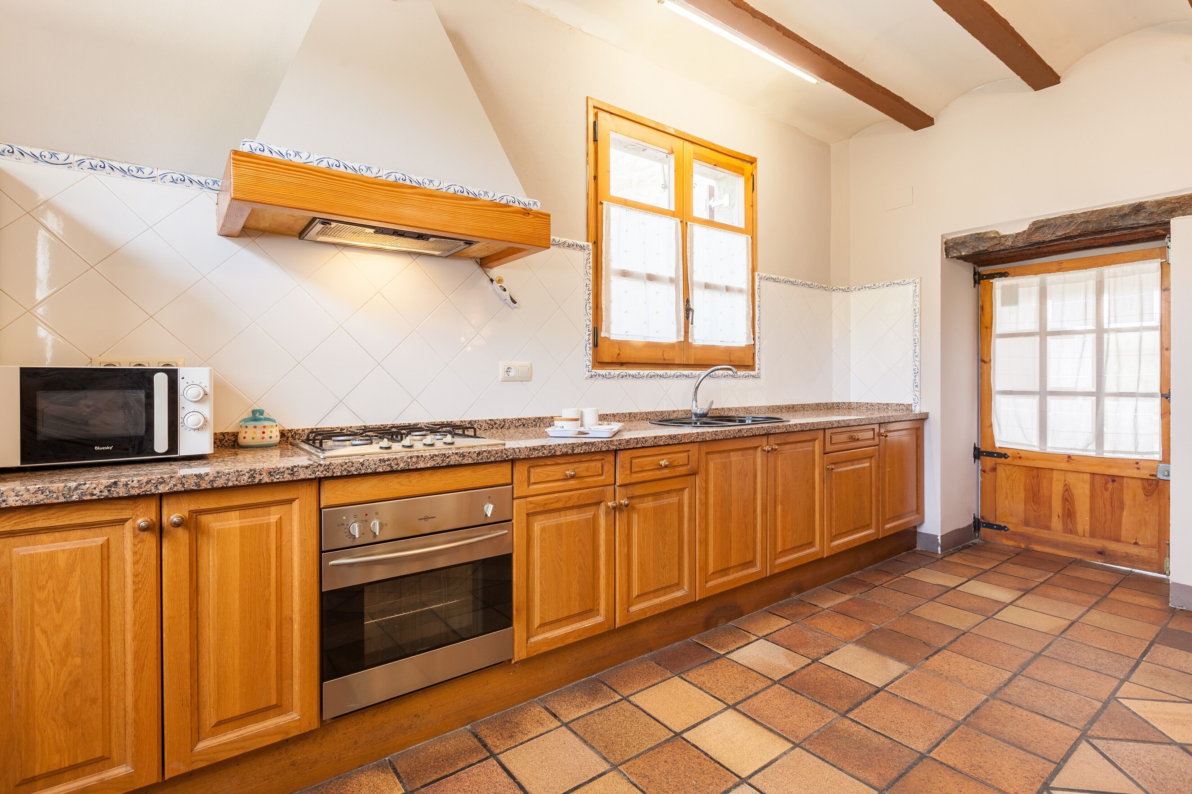 A kitchen with wooden cabinets, a built-in oven, a microwave, and a window with a wooden frame.