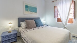 A neatly made bed with a headboard, a bedside table with a lamp, a window with curtains, and a painting on the wall. - Holiday Home 'La Clau Casa Rural ' with Mountain View, Private Terrace and Wi-Fi (Polop)