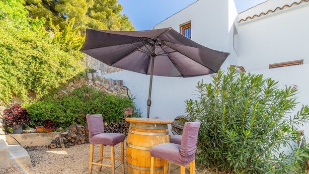 An outdoor seating area with a wooden barrel table, two chairs, and a large umbrella. - Holiday Home 'La Clau Casa Rural ' with Mountain View, Private Terrace and Wi-Fi (Polop)