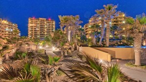 Een nachtzicht van een resort met meerdere hoge gebouwen, palmbomen en verlichte paden.
