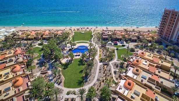 Een resort met een zwembad, palmbomen en een strand.