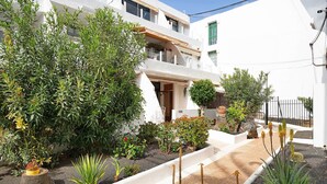 Ein weißes Gebäude mit Balkon, umgeben von verschiedenen Pflanzen und einem kleinen Garten.