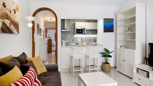 Ein Wohnzimmer mit einer Couch, einem Couchtisch und einer Küchenzeile mit Mikrowelle und Barhocker.