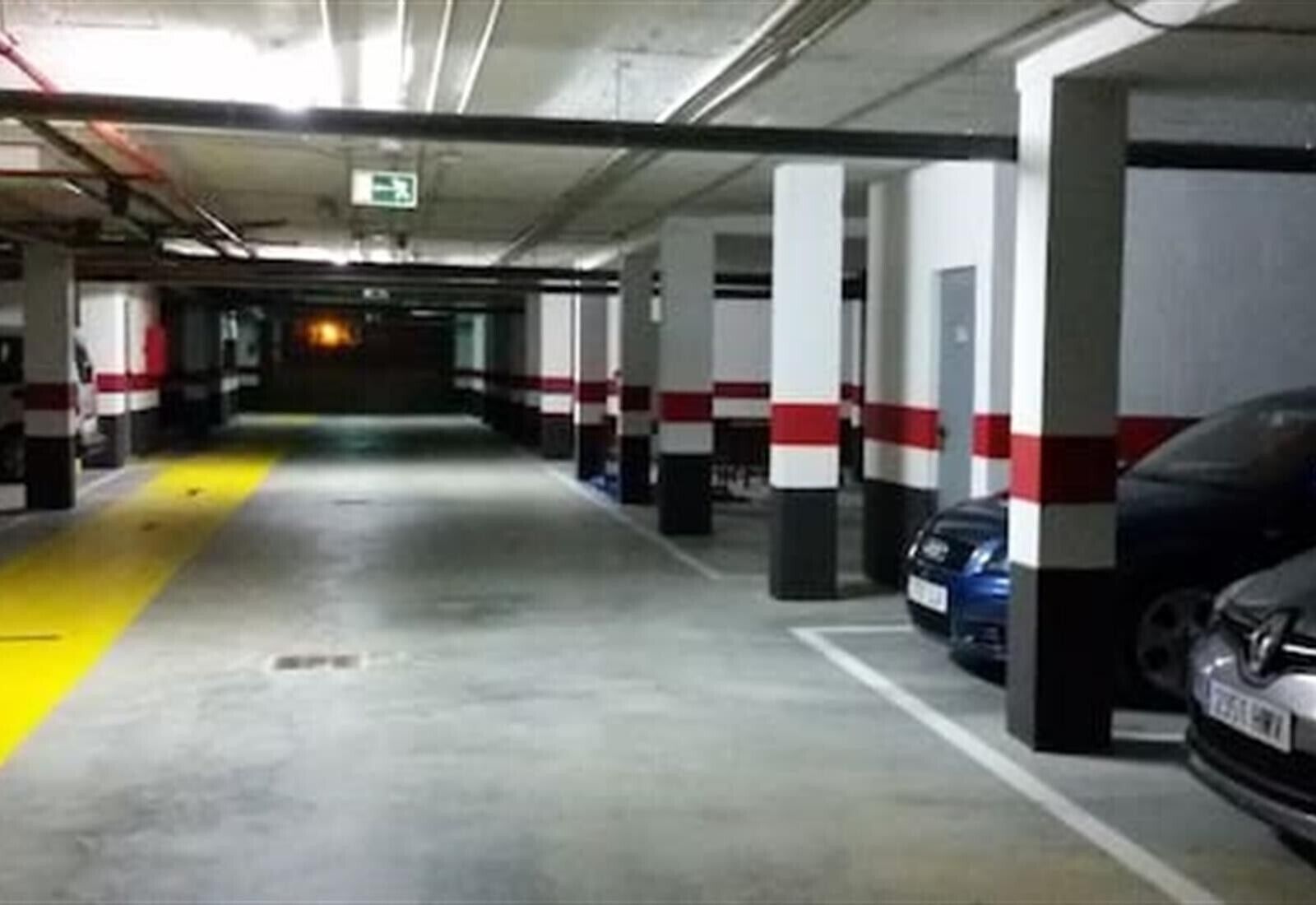 En parkeringskælder med flere etager, betonstolper, gule sikkerhedslinjer og en blå bil parkeret til højre.