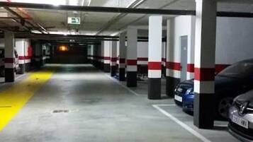 En parkeringskælder med flere etager, betonstolper, gule sikkerhedslinjer og en blå bil parkeret til højre.