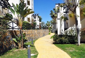 Un sendero conduce a un edificio con un muro de piedra y plantas tropicales.