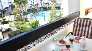 A balcony with a dining table set for breakfast, overlooking a pool and resort buildings. - Apartment 'Residencial Duquesa Fase I' with Terraces, Shared Pools & Wi-Fi (Manilva)