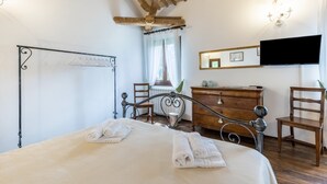 Une chambre à coucher avec un lit, une commode, une chaise, un téléviseur et une fenêtre avec des rideaux.
