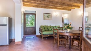 Une cuisine équipée d’un réfrigérateur, un coin repas avec une table et des chaises en bois, un canapé vert et une fenêtre donnant sur un paysage verdoyant.