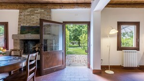 Une pièce avec une cheminée en briques, une table à manger avec des chaises, un lampadaire et une vue sur un jardin par une porte ouverte.