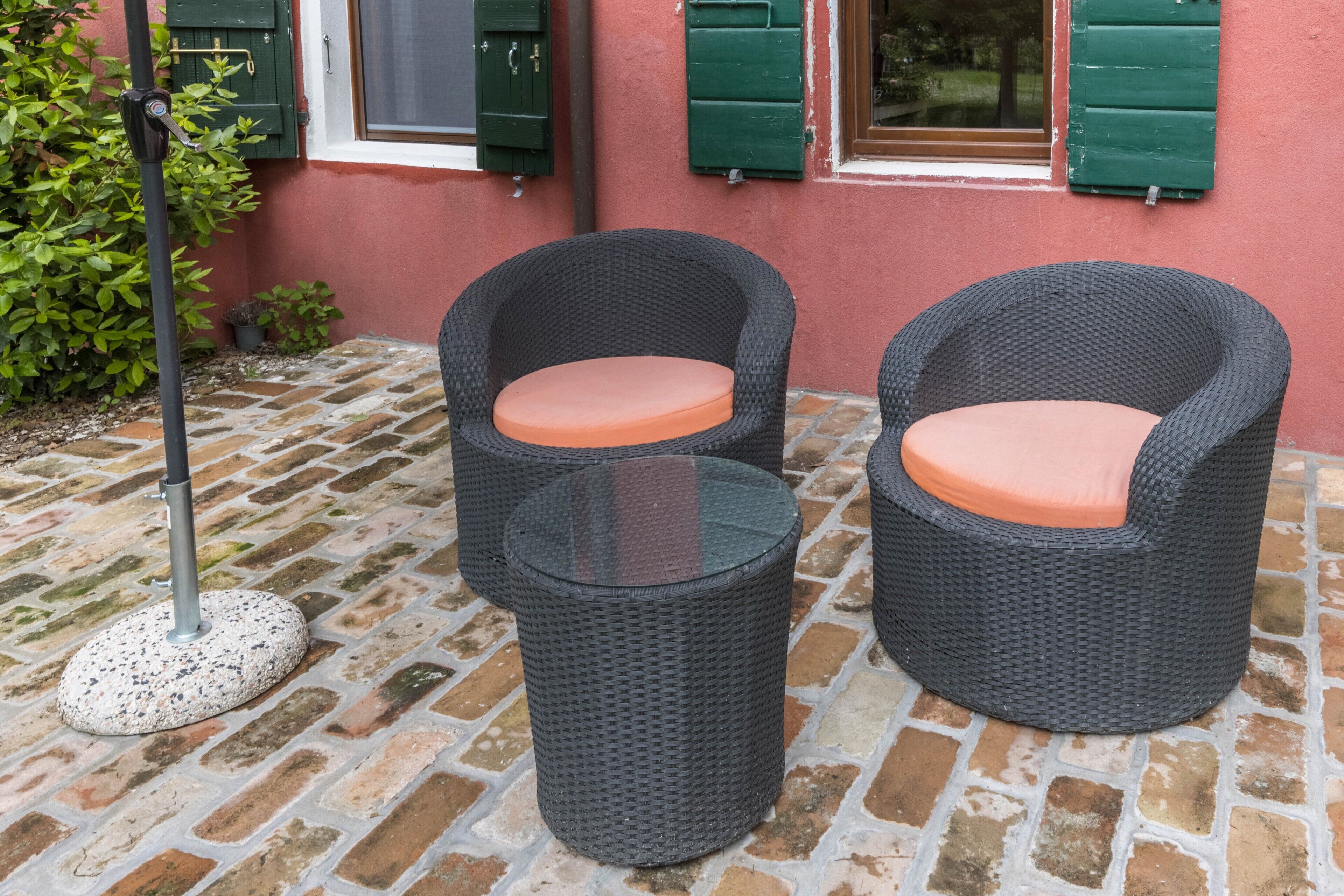 Due poltrone in vimini con cuscini arancioni e un tavolino di vetro su un patio in mattoni.