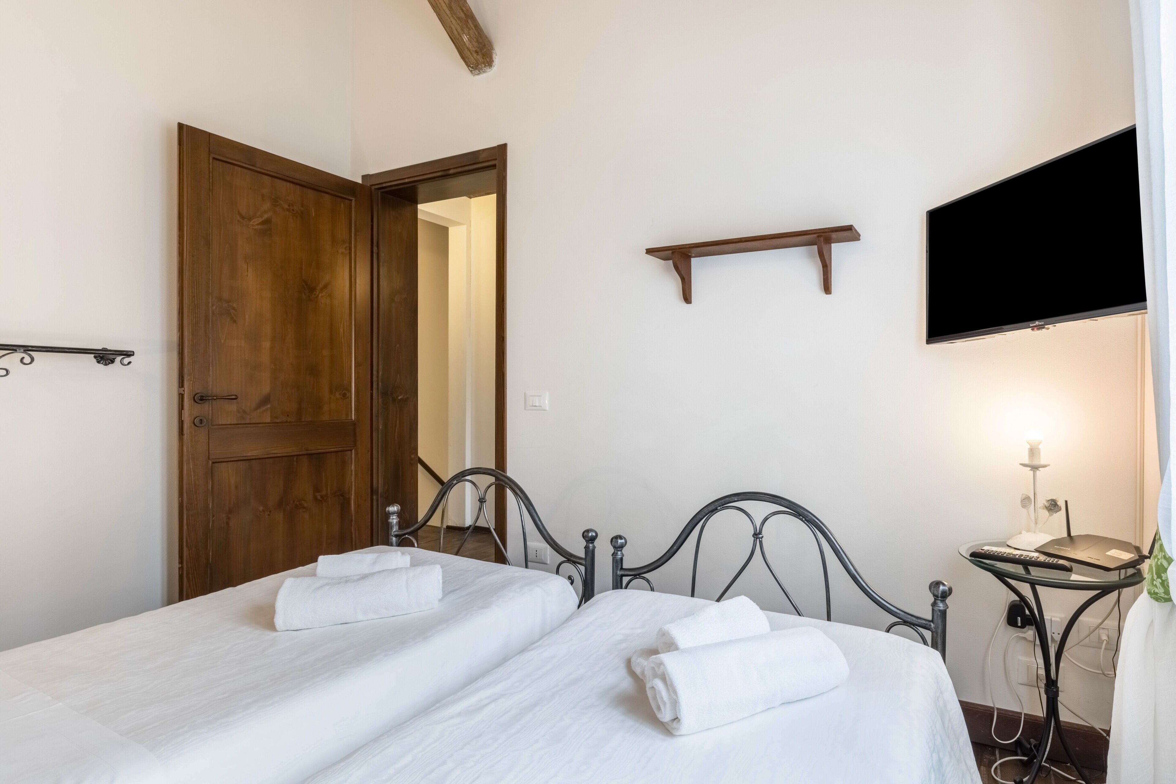 Un dormitorio con dos camas, una puerta de madera, un televisor y una mesita de noche con lámpara.