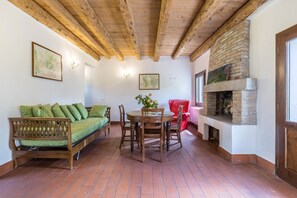 A room with a wooden ceiling, a brick fireplace, a green sofa, a dining table with chairs, and a red chair. - 'Tenuta Ca' Zen - Cottage Casetta' with Shared Pool, Wi-Fi and Air Conditioning (Taglio di Po)
