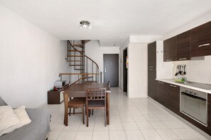Une cuisine moderne avec des meubles de couleur sombre en bois, un four encastré et un coin repas comprenant une table et des chaises en bois.