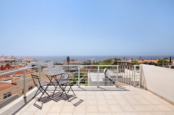 A rooftop terrace with a view of the sea, a metal railing, and a folding chair.