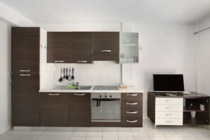 Une cuisine moderne avec des meubles de couleur sombre, un four encastré, un évier et un petit bureau avec un ordinateur portable.