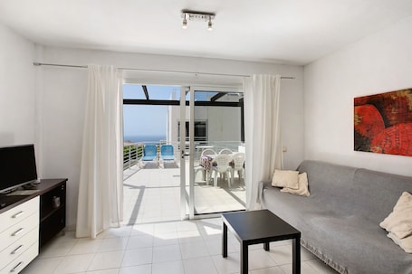 A modern living room with a sofa, a TV, and a balcony with outdoor furniture.
