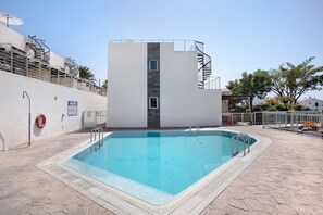 Une piscine avec un escalier menant à un bâtiment, une bouée de sauvetage et un ciel dégagé.