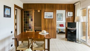 Une pièce avec un mur lambrissé en bois, une table à manger avec des chaises, un téléviseur et un lit près d’une fenêtre.