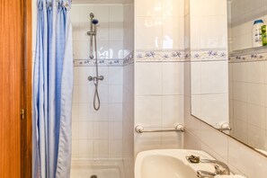 Een badkamer met een douche, een wastafel, een spiegel en een deur.