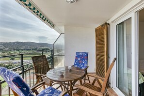 Een balkon met een tafel en stoelen, uitzicht op het landschap en een gebouw in de verte.