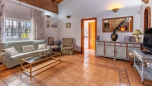 A living room with a sofa, armchair, coffee table, TV, cabinet, and a door leading to another room. - Holiday Home 'Villa Verde' with Mountain View, Private Pool and Wi-Fi (Nigüelas)