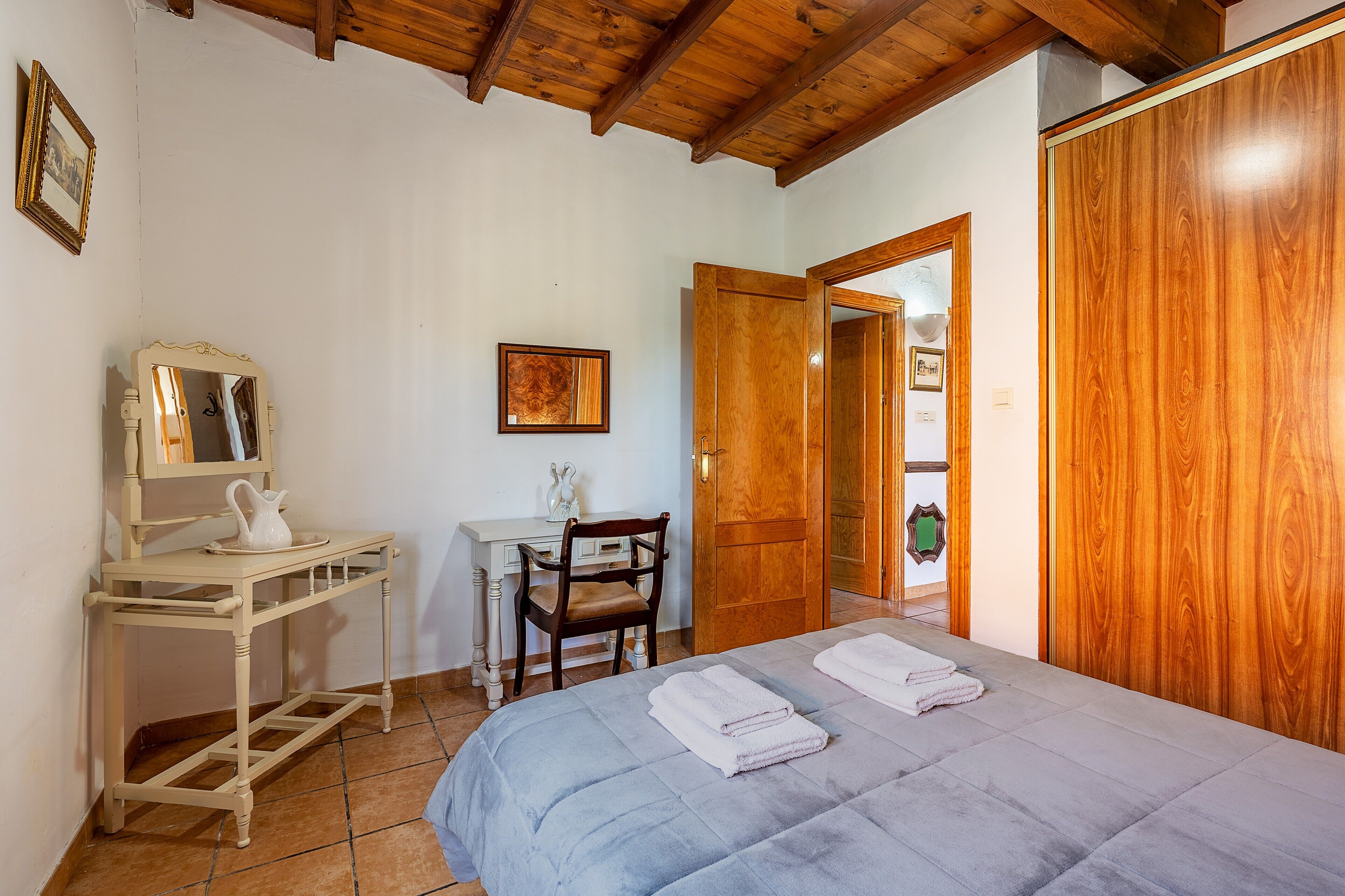 Un dormitorio con cama, escritorio, silla, armario y una puerta que da a otra habitación.