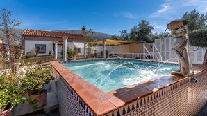 A swimming pool with a tiled edge, a statue, and a building with a red roof in the background. - Holiday Home 'Villa Verde' with Mountain View, Private Pool and Wi-Fi (Nigüelas)