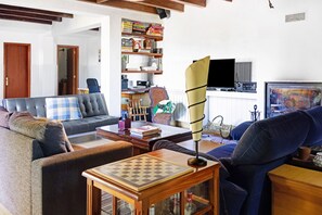 Un salon comprenant un canapé, une table basse avec un jeu d’échecs, une bibliothèque, un téléviseur et un tableau.