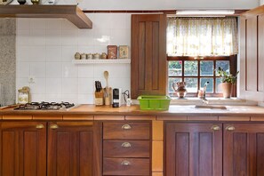 Une cuisine avec des meubles en bois, une cuisinière à gaz, un évier et une fenêtre donnant sur un paysage agréable.