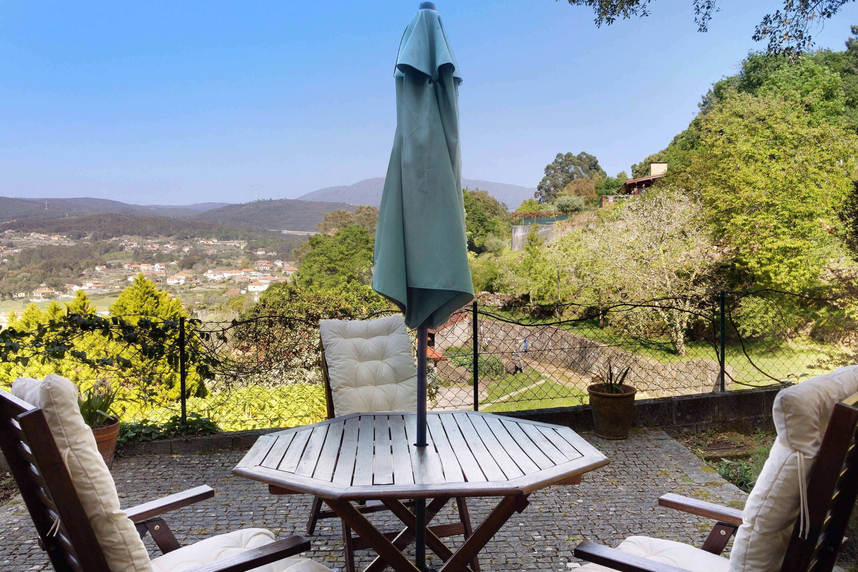 Une terrasse avec une table et des chaises, un parasol vert et une vue sur un paysage vallonné.