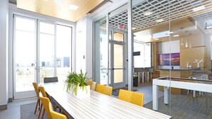 A modern conference room with a long table, yellow chairs, a potted plant, and large windows offering a city view. - Elan Menlo (Menlo Park)