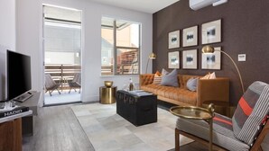 A modern living room with a sofa, armchair, coffee table, and a TV. There is a sliding glass door leading to an outdoor area with chairs. - Elan Menlo (Menlo Park)