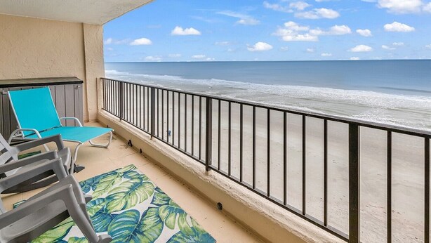 Un balcon donnant sur la plage, avec une balustrade et deux fauteuils bleus confortables.
