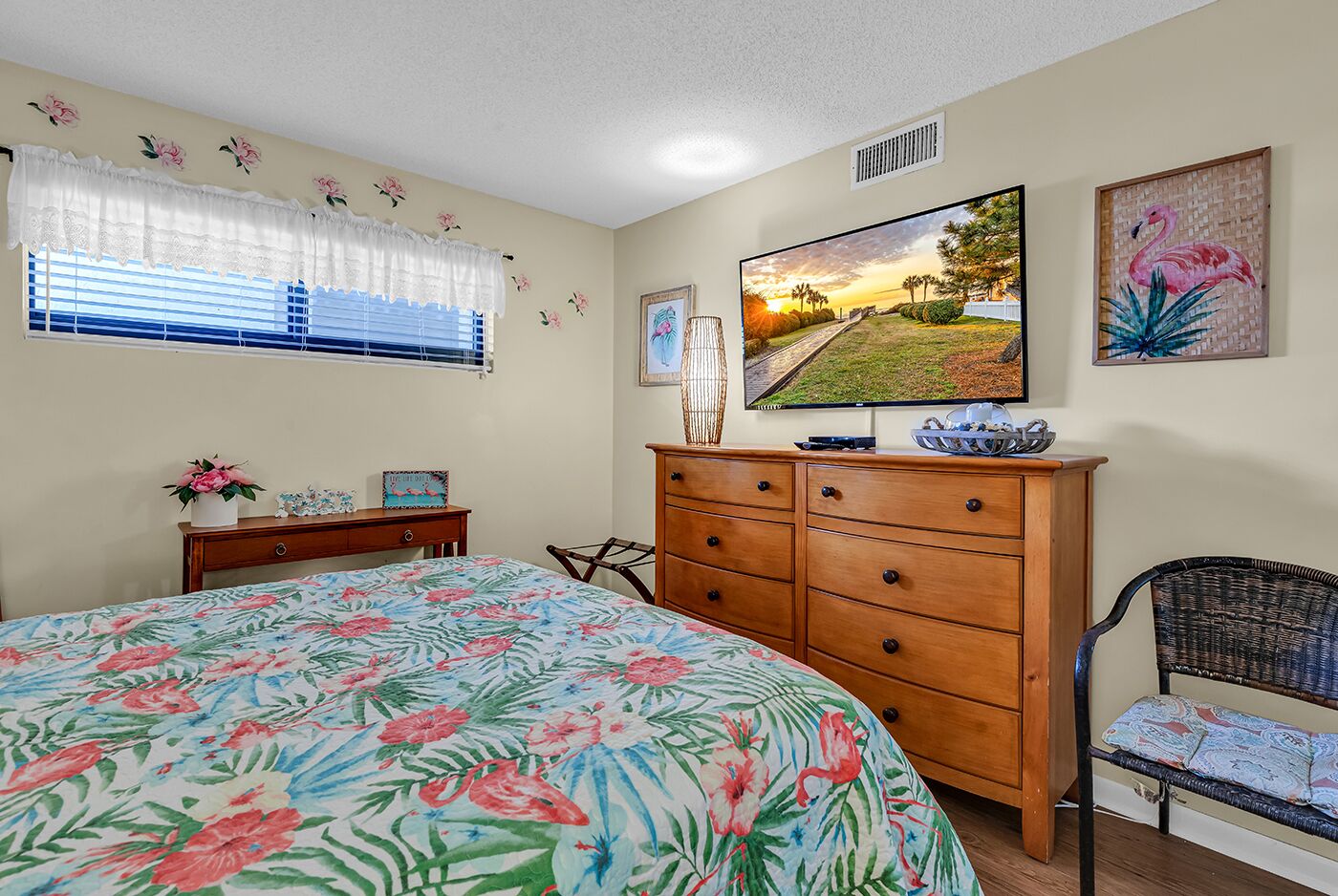 A bedroom with a bed, dresser, chair, and a TV on the wall.