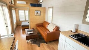 Eine kompakte, moderne Hütte mit Holzinnenausstattung, einem Sofa, einem Esstisch und einer Küchenzeile.