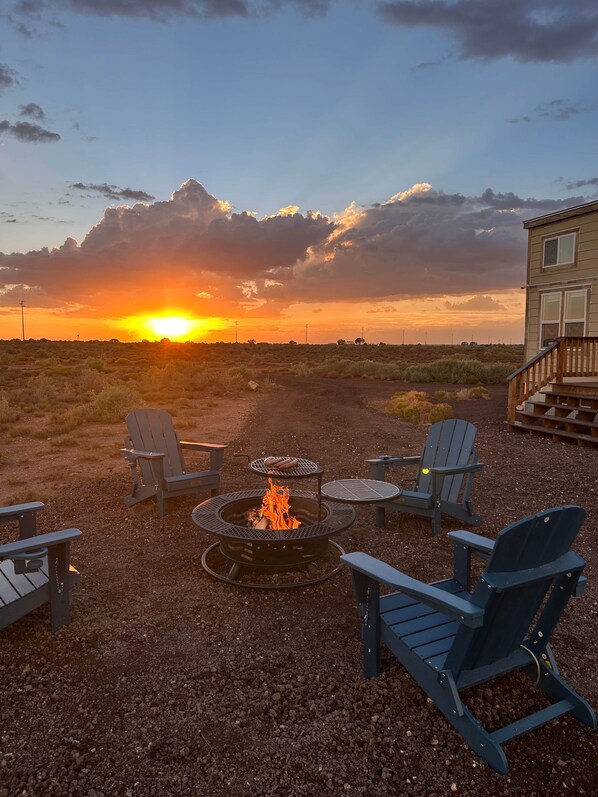 A fire pit with chairs around it, a building in the background, and a sunset.