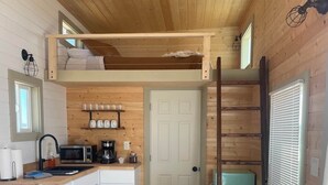 Eine kompakte Küche mit Holzschränken, einer Mikrowelle und einer Kaffeemaschine. Es gibt einen Essbereich mit Tisch und Stühlen.