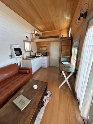 A compact living space with a kitchenette, a sofa, a coffee table, and a ladder.
