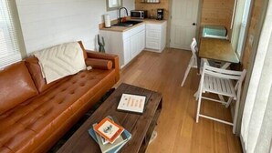 Ein gemütlicher Wohnbereich mit Sofa, Couchtisch, Esstisch mit Stühlen, Küchenzeile und kleinem Fenster.