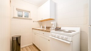 Una cocina compacta con alacenas blancas, estufa, cafetera y un cubo de basura.