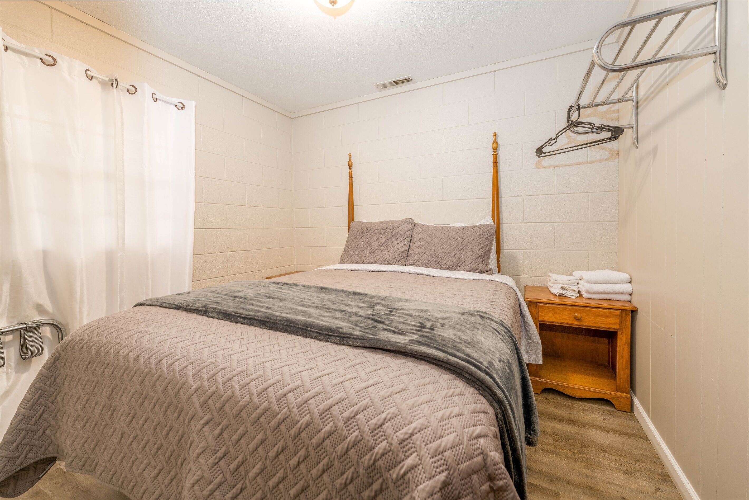 A bedroom with a bed, a wooden nightstand, a towel rack, and a shower curtain.